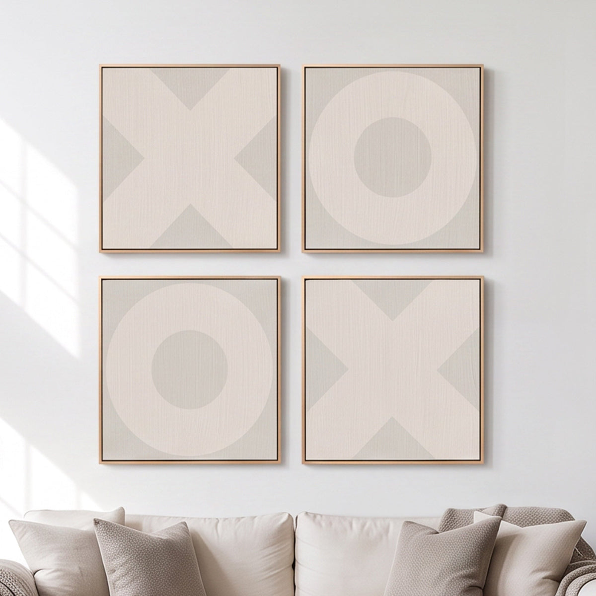 Four framed square wall art prints arranged in a 2x2 grid above a sofa. Each print features a large geometric X or O motif in soft beige and light gray tones with a thin natural wood frame, set against a white wall with soft window light shadows.